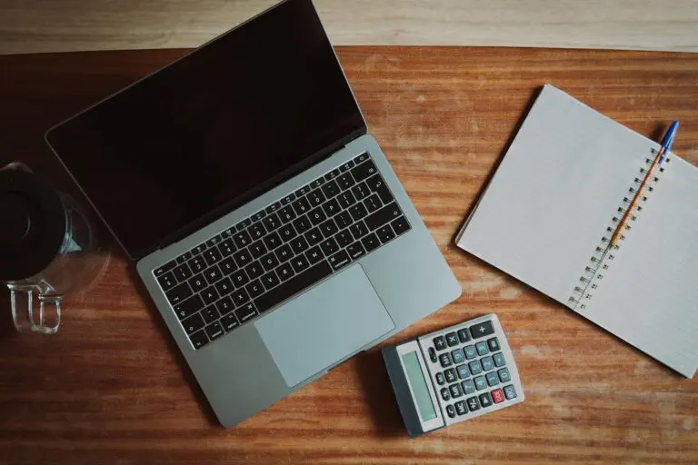 A laptop, notebook and calculator on a wooden desk